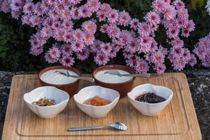 A wooden board with three bowls of yogurt and two bowls of fruit compote, set against a backdrop of pink flowers. - Anerada Inn Suites Pool & Spa | Blue Suite (Megalo chorio)