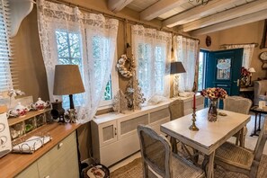 A cozy room with a dining table, chairs, a window with lace curtains, and a blue door. - Anerada Inn Suites Pool & Spa | Garden House (Megalo chorio)