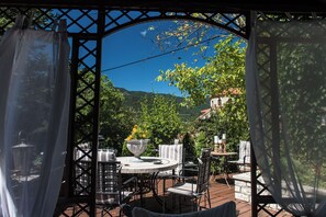 An outdoor patio with a round table and chairs, surrounded by a wooden deck and a pergola structure. - Anerada Inn Suites Pool & Spa | Garden House (Megalo chorio)