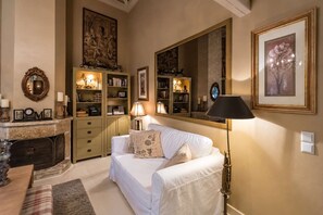 A cozy living room with a white sofa, a fireplace, bookshelves, and a large mirror. - Anerada Inn Suites Pool & Spa | Garden House (Megalo chorio)