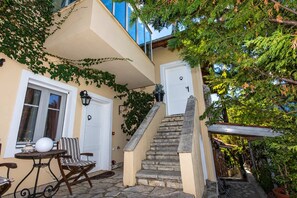 Ein Gebäude mit einer Steintreppe, die zu einer Tür führt, einem Tisch mit Stühlen davor und einem Fenster mit Vorhängen.