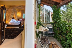 A bedroom with a canopy bed, a small table with a chair, and a view of a garden with a wooden deck. - Anerada Inn Suites Pool & Spa | Master Suite (Megalo chorio)