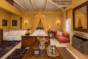 A hotel room with a four-poster bed, a sofa, a fireplace, and a dining table with a tray. - Anerada Inn Suites Pool & Spa | Master Suite (Megalo chorio)