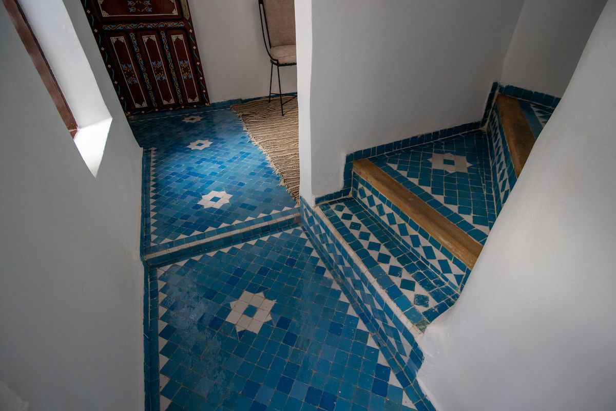Un escalier recouvert de carreaux bleus à motifs, menant à une pièce dont la porte est également ornée de motifs.