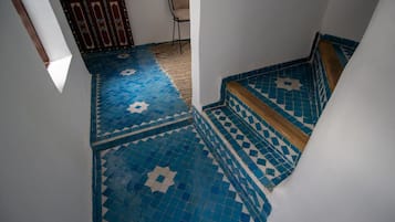 Un escalier recouvert de carreaux bleus à motifs, menant à une pièce dont la porte est également ornée de motifs.