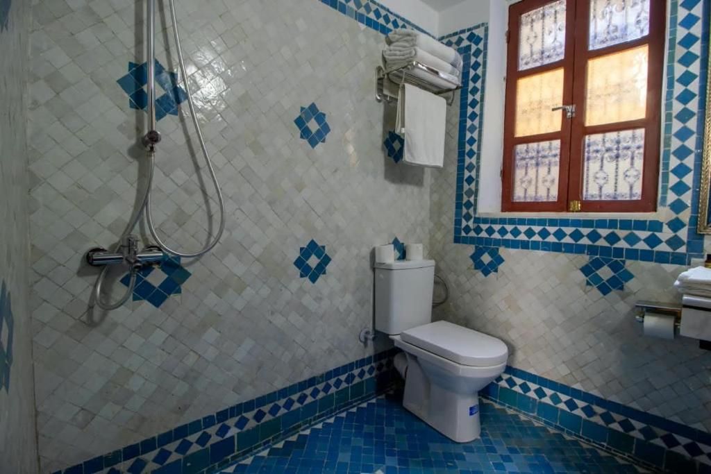 A bathroom with a toilet, a shower, and a window with a decorative frame.