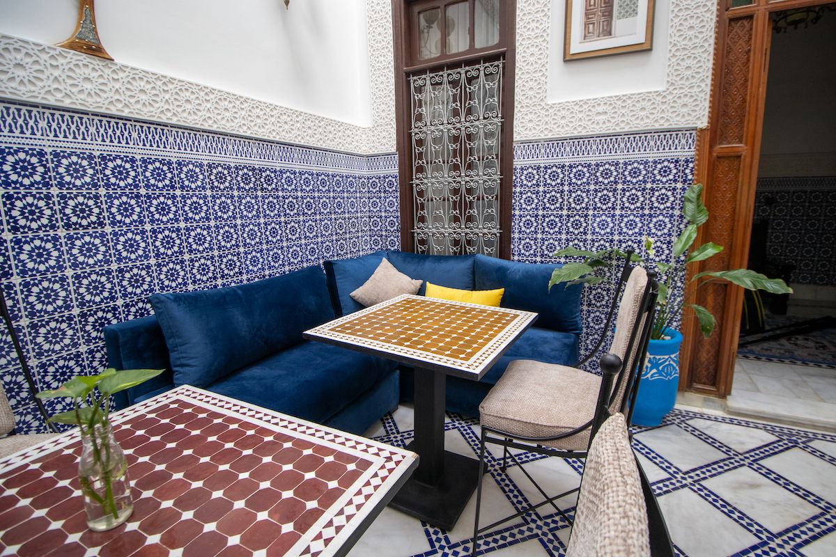 A cozy seating area with a blue sofa, a small table, and a chair, surrounded by intricately patterned walls and a tiled floor.