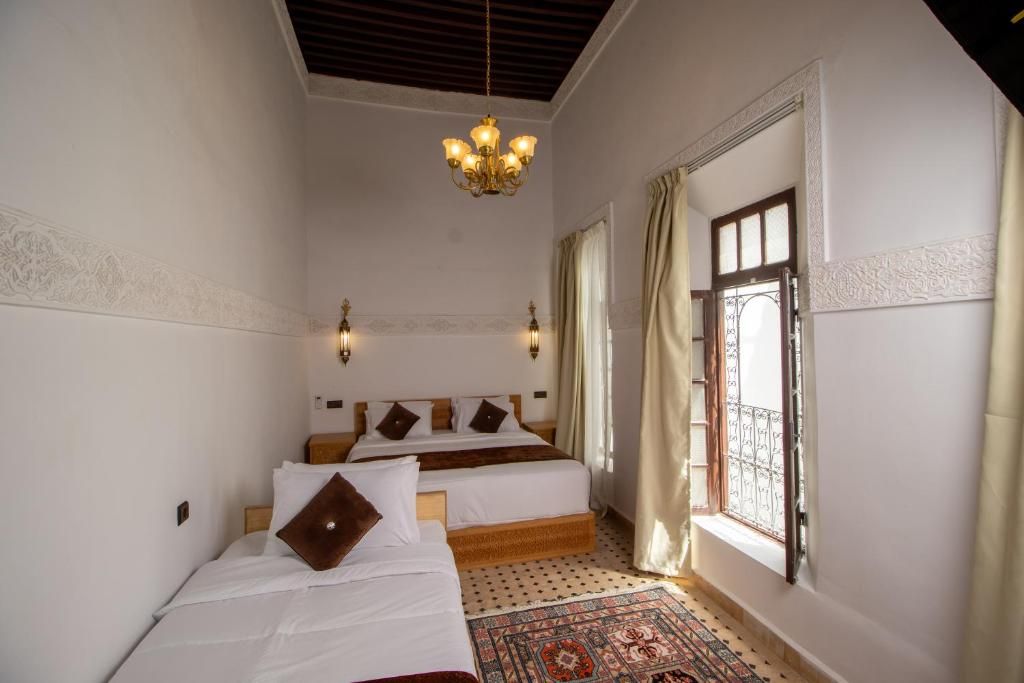A hotel room with two beds, a chandelier, a patterned rug, and a window with curtains.