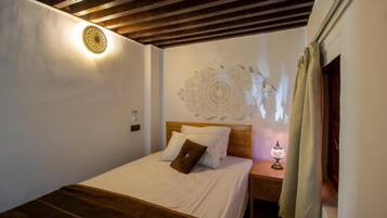 A bedroom with a wooden headboard, a bed with white bedding, a nightstand with a lamp, and a decorative wall piece.
