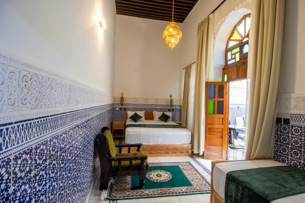 A room with a bed, a chair, a patterned rug, and a window with curtains.
