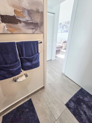 A bathroom with a towel rack holding two towels, a toilet paper holder, and a rug on the floor. - Luxury Apartment with shared pool (Miami)