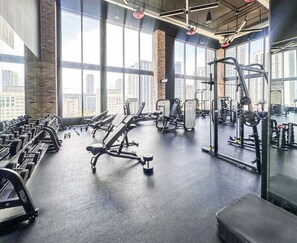 A gym with various exercise equipment, large windows, and a city view. - Luxury Apartment with shared pool (Miami)