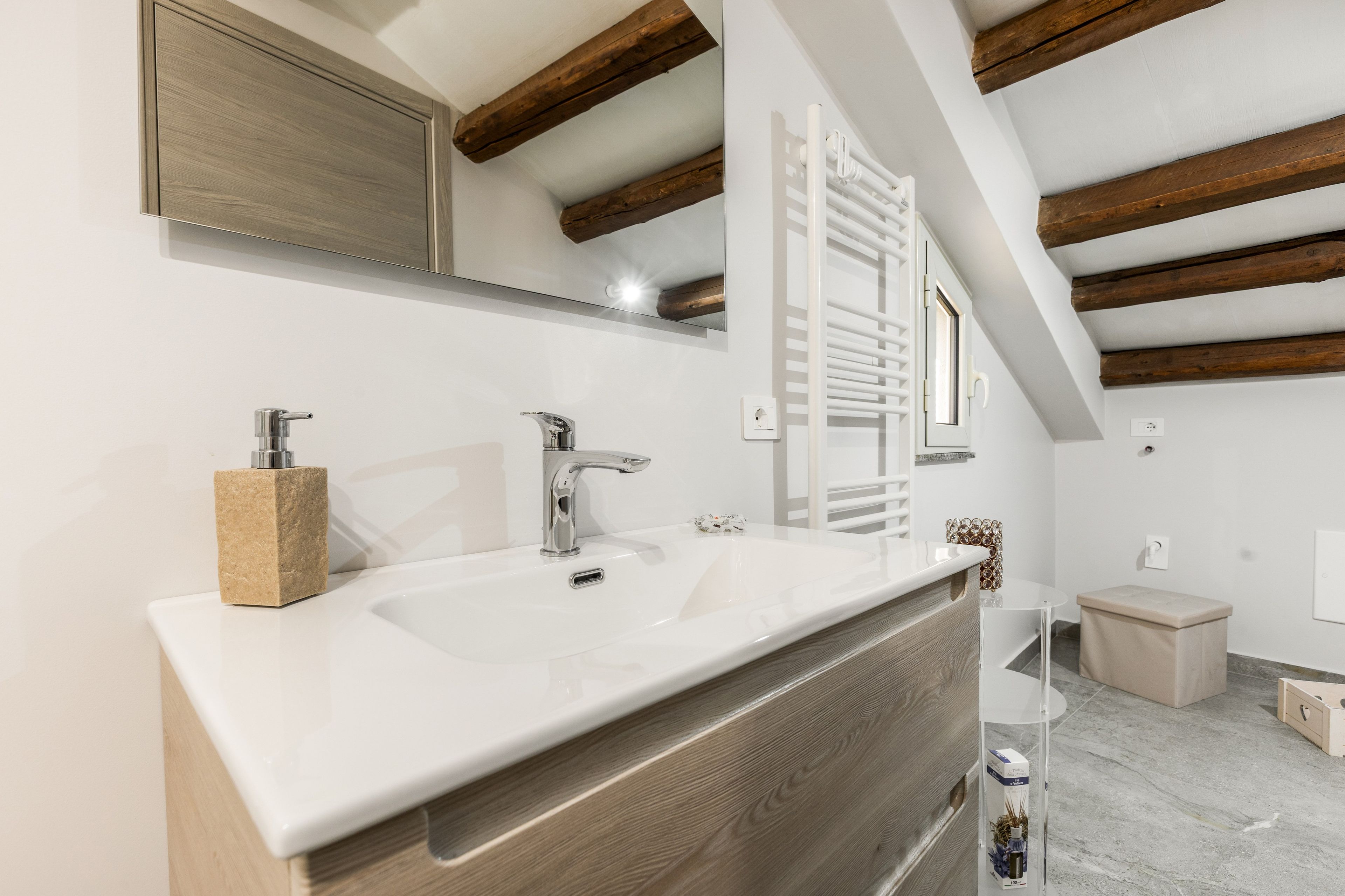 Een moderne badkamer met een witte wastafel, twee kranen, een houten kastje, een spiegel en een handdoekhouder.