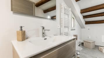 Een moderne badkamer met een witte wastafel, twee kranen, een houten kastje, een spiegel en een handdoekhouder.