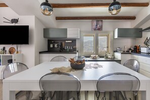 A modern kitchen with a central island, pendant lighting, and a dining area with chairs.