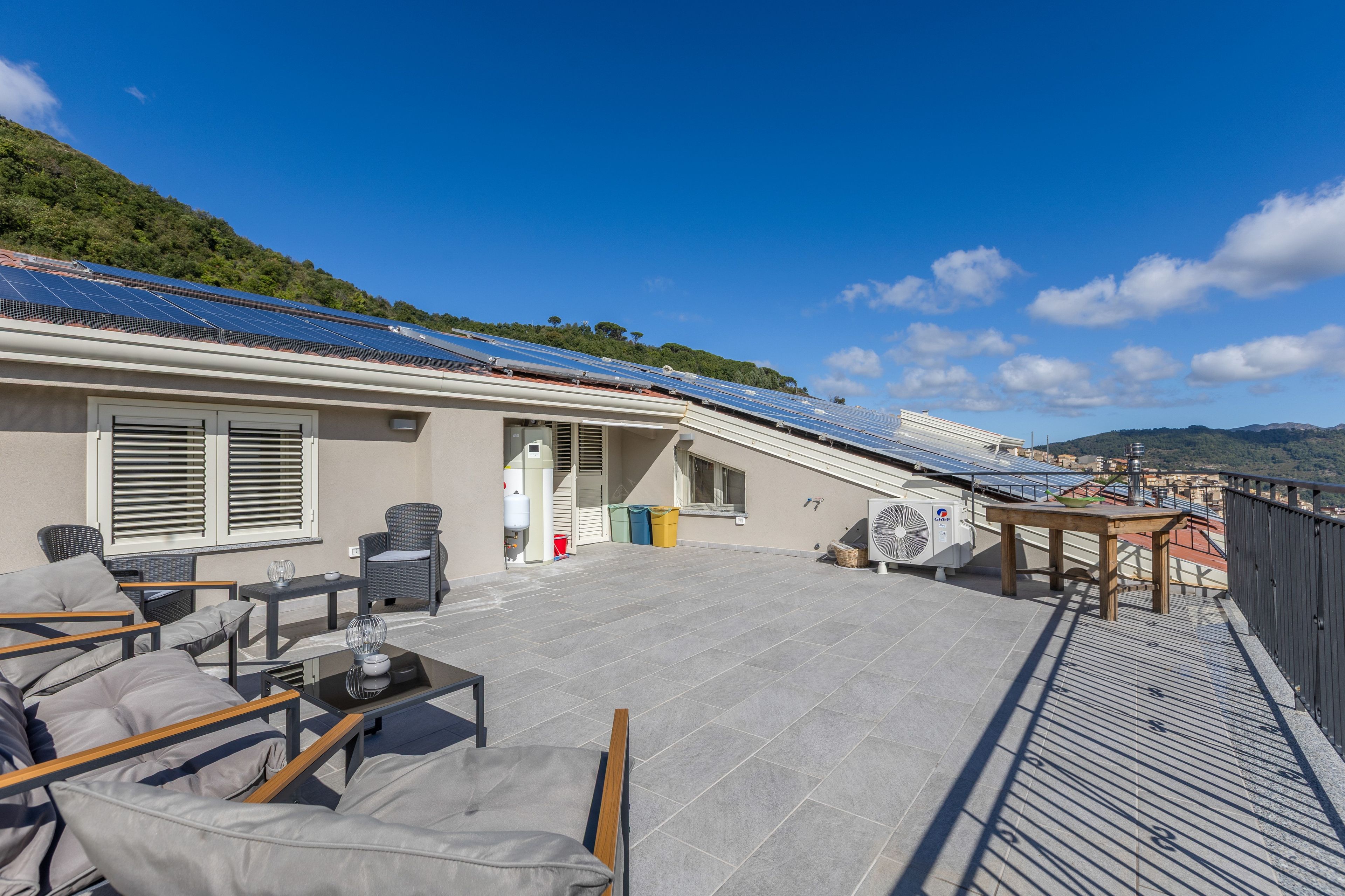 En takterrass med solpaneler, utemöbler och utsikt över det omgivande landskapet.