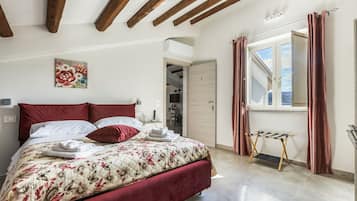 Een slaapkamer met een bed, een schilderij, een raam met gordijnen en een deur naar een andere kamer.