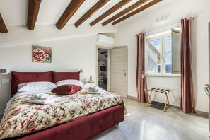 A bedroom with a bed, a painting, a window with curtains, and a door leading to another room.