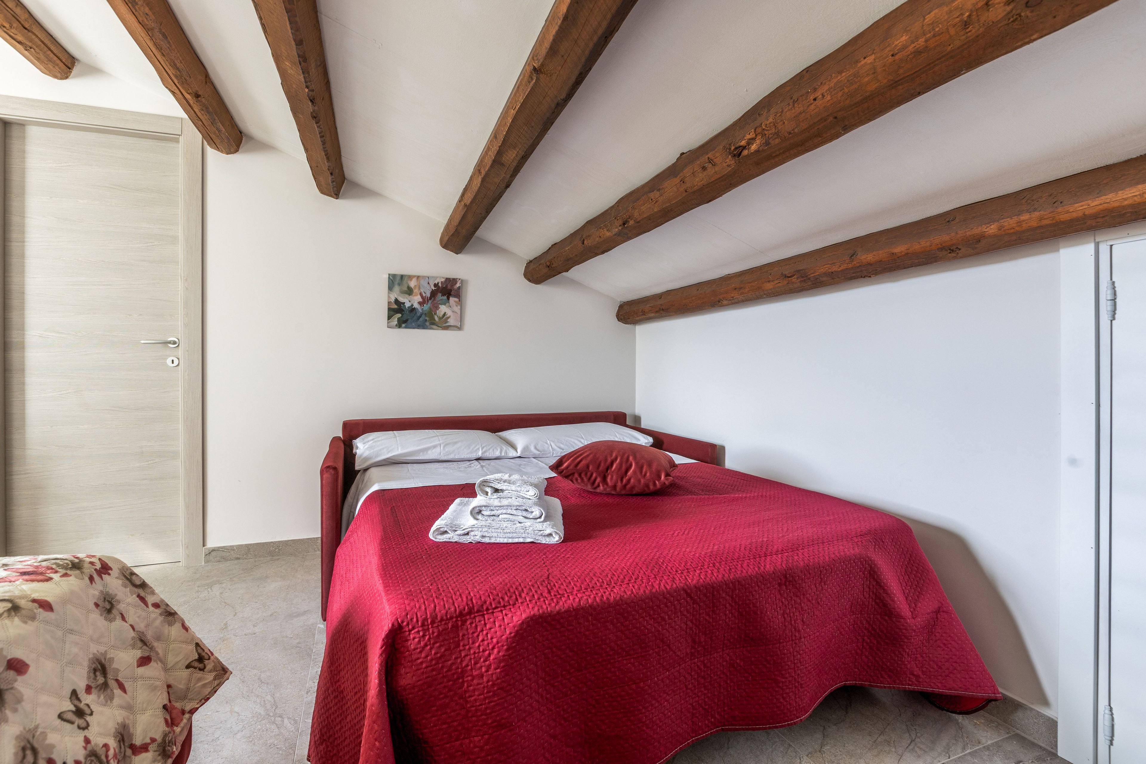 A bedroom with a bed, a door, and a small painting on the wall.