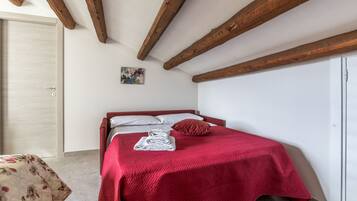 A bedroom with a bed, a door, and a small painting on the wall.