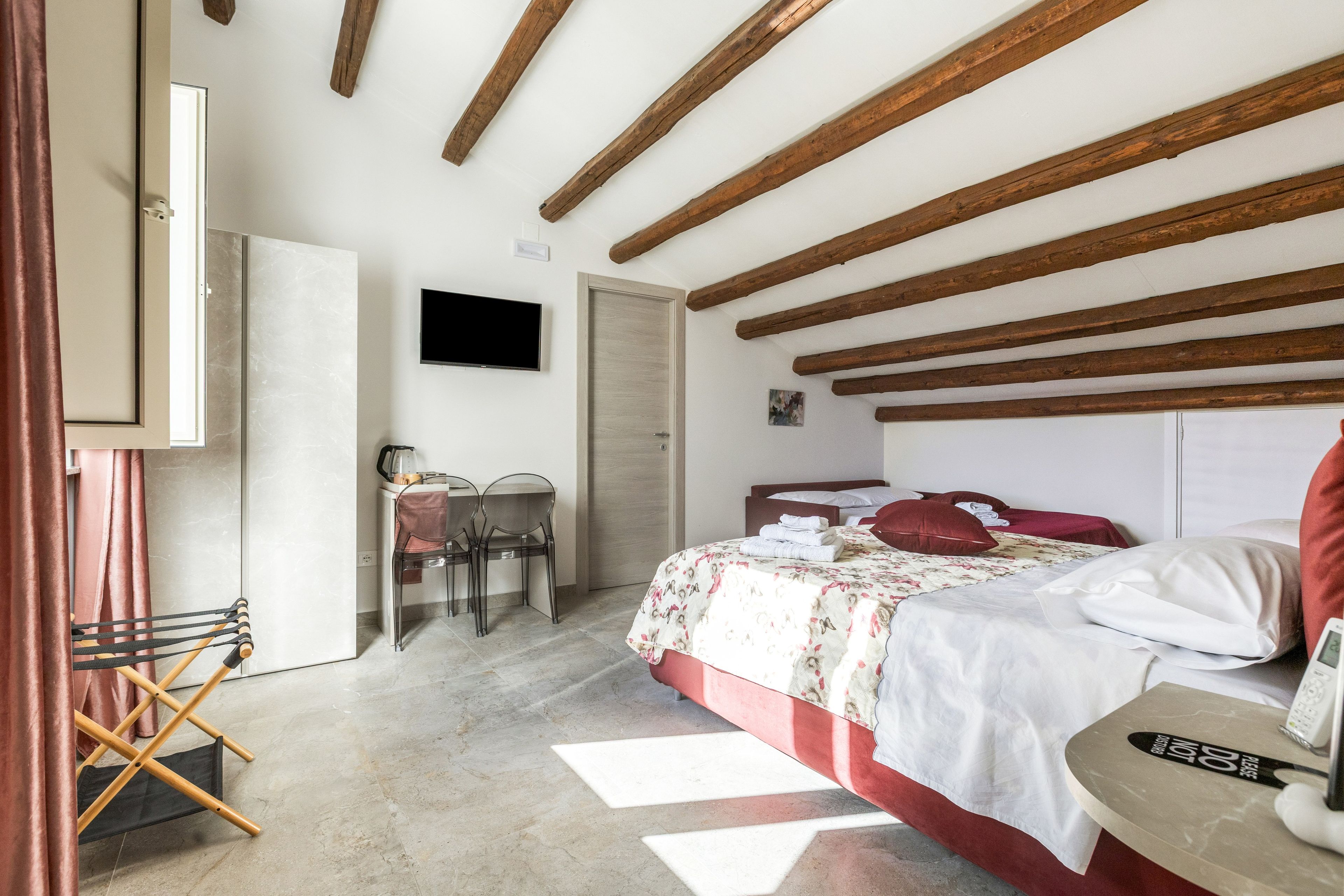 Un dormitorio con cama, escritorio, silla, televisor y puerta.