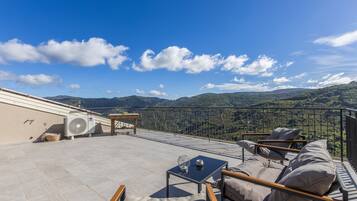 A rooftop terrace with a view of the mountains, a table with chairs, and an air conditioning unit.