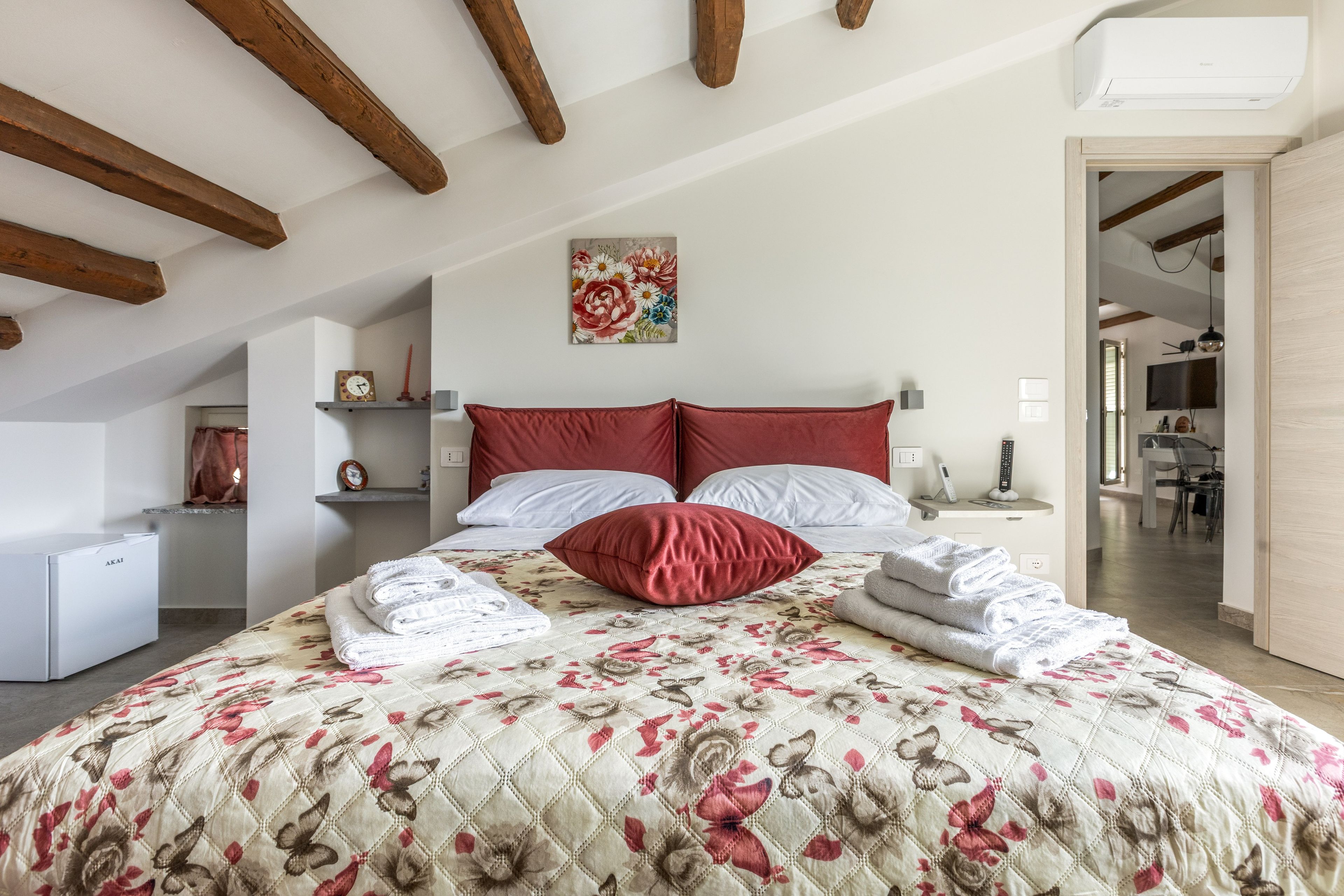 Een slaapkamer met een bed, kussens, een sprei, een nachtkastje, een wandklok, een plank met decoratieve voorwerpen en een schilderij.