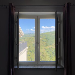 Een kamer met een grote schuifpui die uitkomt op een balkon met uitzicht op een groen landschap.