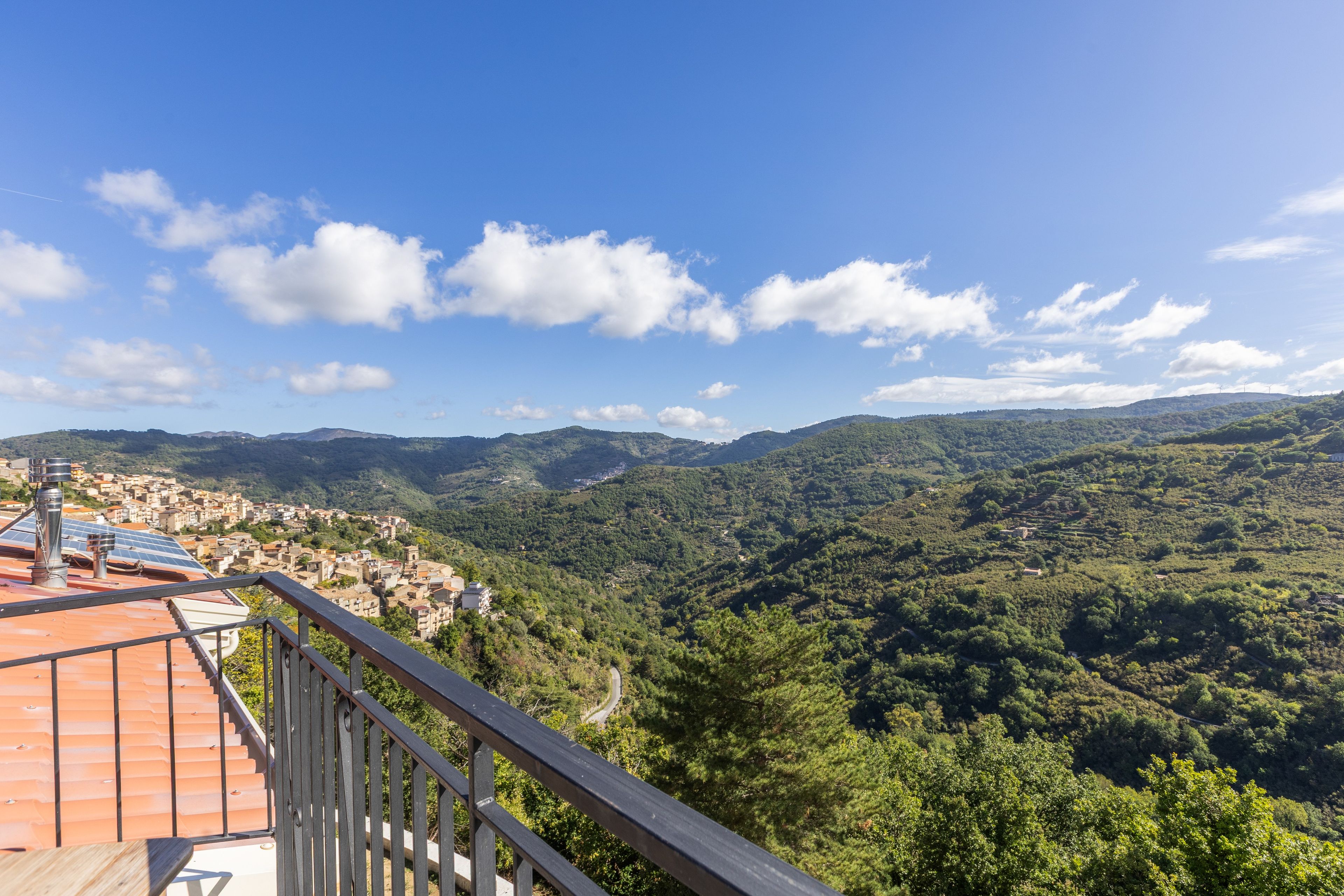 Un balcone con vista su una città e colline boscose.