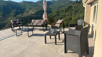 A terrace with outdoor furniture, a table, and an umbrella, overlooking a mountainous landscape.