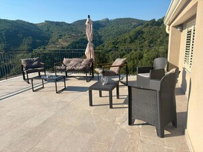 Una terraza con mobiliario exterior, una mesa y un paraguas, con vistas a un paisaje montañoso.