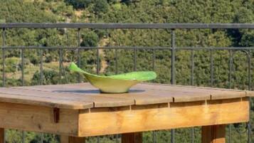 Une table en bois sur laquelle est posée une coupe verte, le tout se détachant sur un fond composé d’une rambarde métallique et d’un paysage vallonné parsemé d’éoliennes.