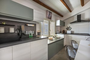A modern kitchen with a built-in oven, a coffee machine, and a window with blinds.