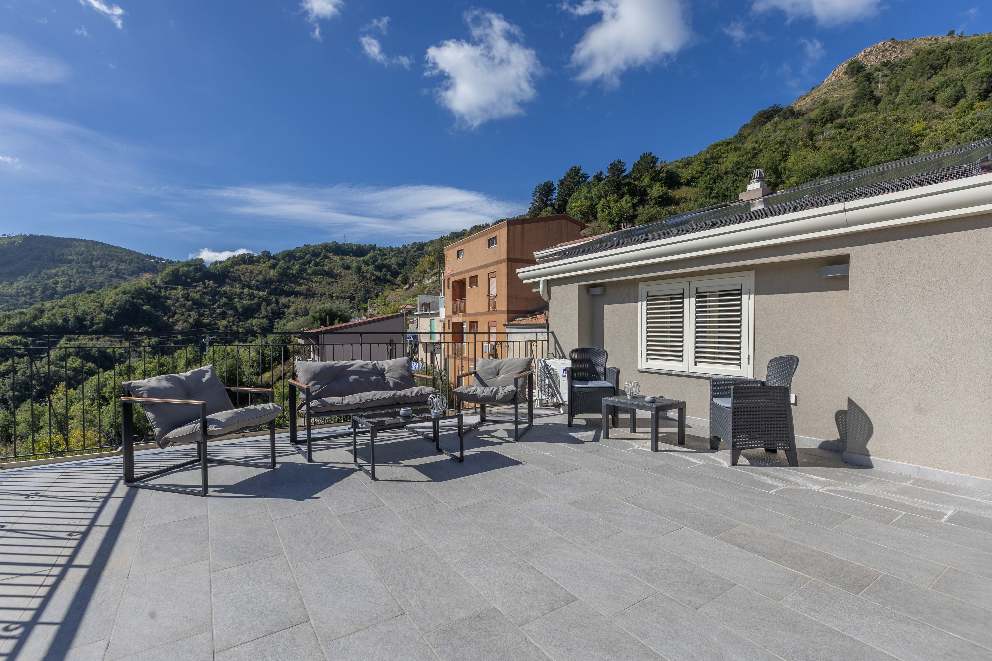 A terrace with outdoor furniture, a view of a hillside, and a building with a sloped roof.