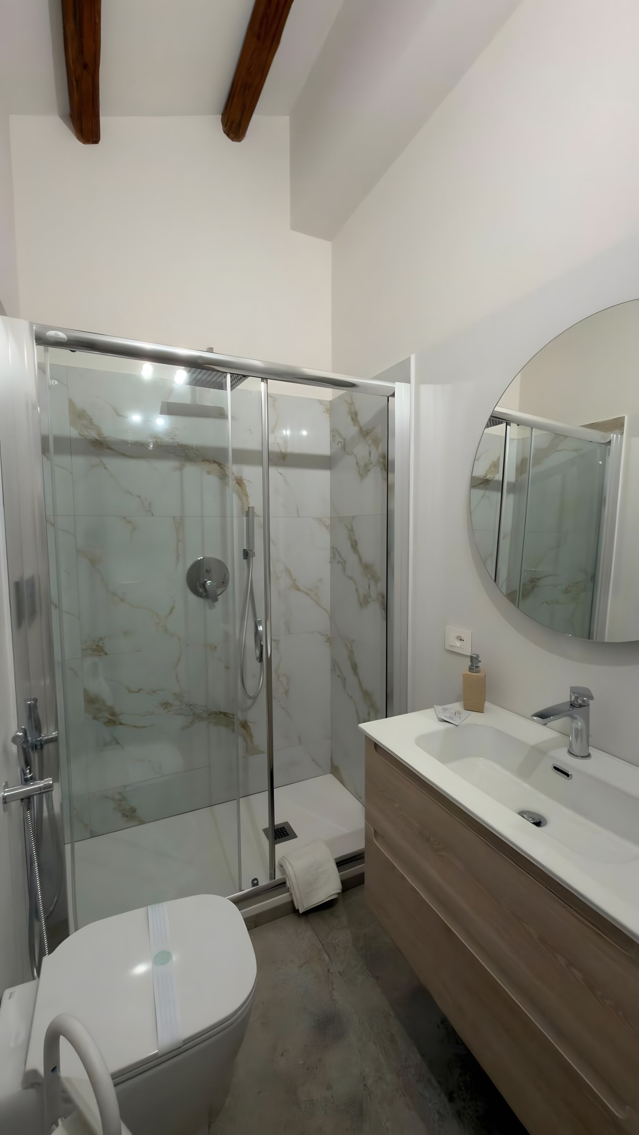 Une salle de bain moderne avec une douche à parois de verre, des toilettes blanches et un meuble-lavabo en bois avec un évier.