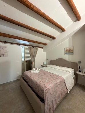 A bedroom with a bed, a nightstand, a wall-mounted clock, and a painting. - Guest House 'Casa Malida - Guest House Beige' (Ucria)