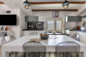 A modern kitchen with a central island, pendant lighting, and a dining area with chairs.