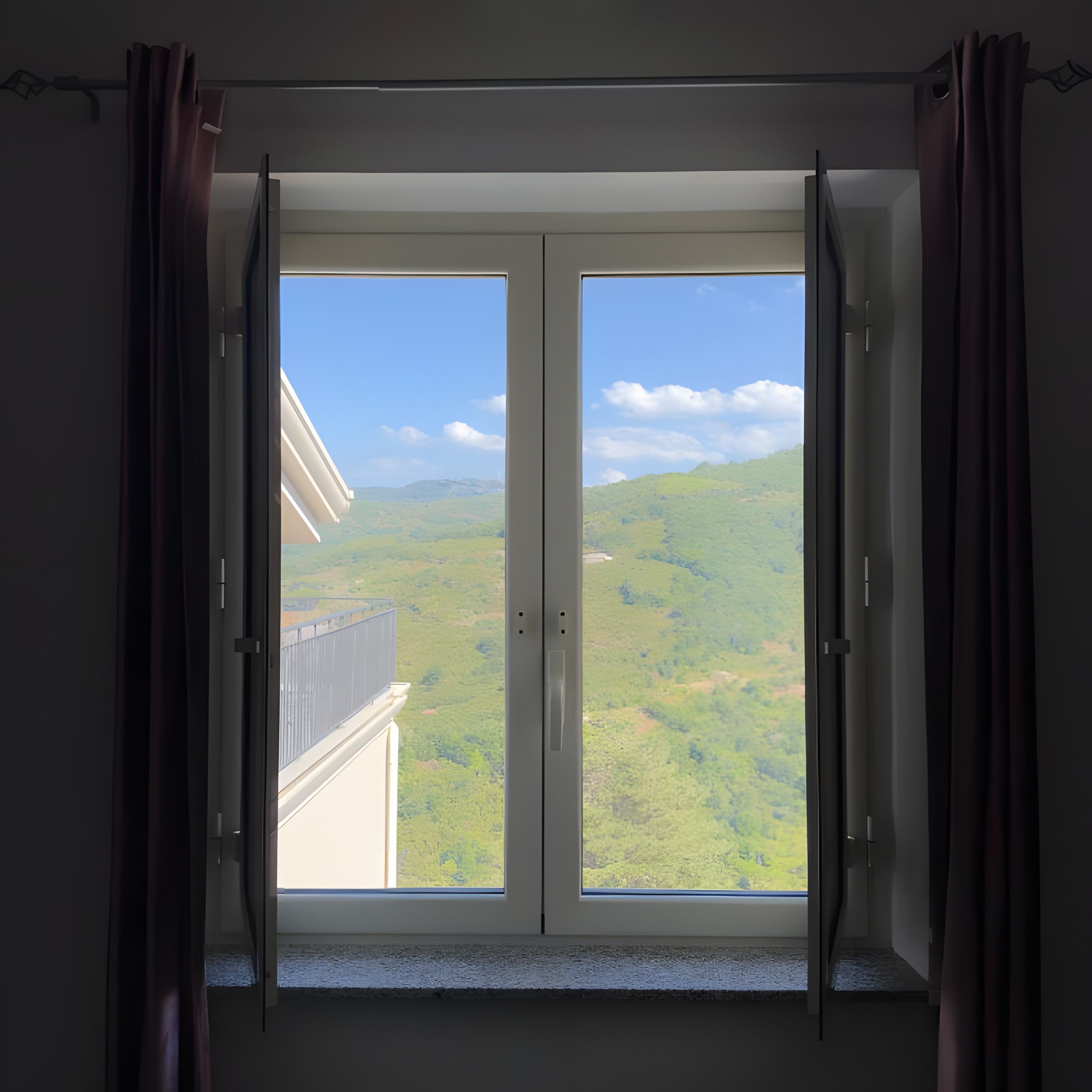 Ein Zimmer mit einer großen Schiebeglastür, die auf einen Balkon mit Blick auf eine grüne Landschaft und Hügel führt.