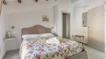A bedroom with a bed, a nightstand, a bedside table, a wall-mounted clock, a door, and a mirror.