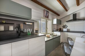 A modern kitchen with a built-in oven, a coffee machine, and a window with blinds.