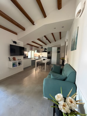 A modern living room with a sofa, a TV mounted on the wall, and a kitchen in the background. - Guest House 'Casa Malida - Guest House Beige' (Ucria)