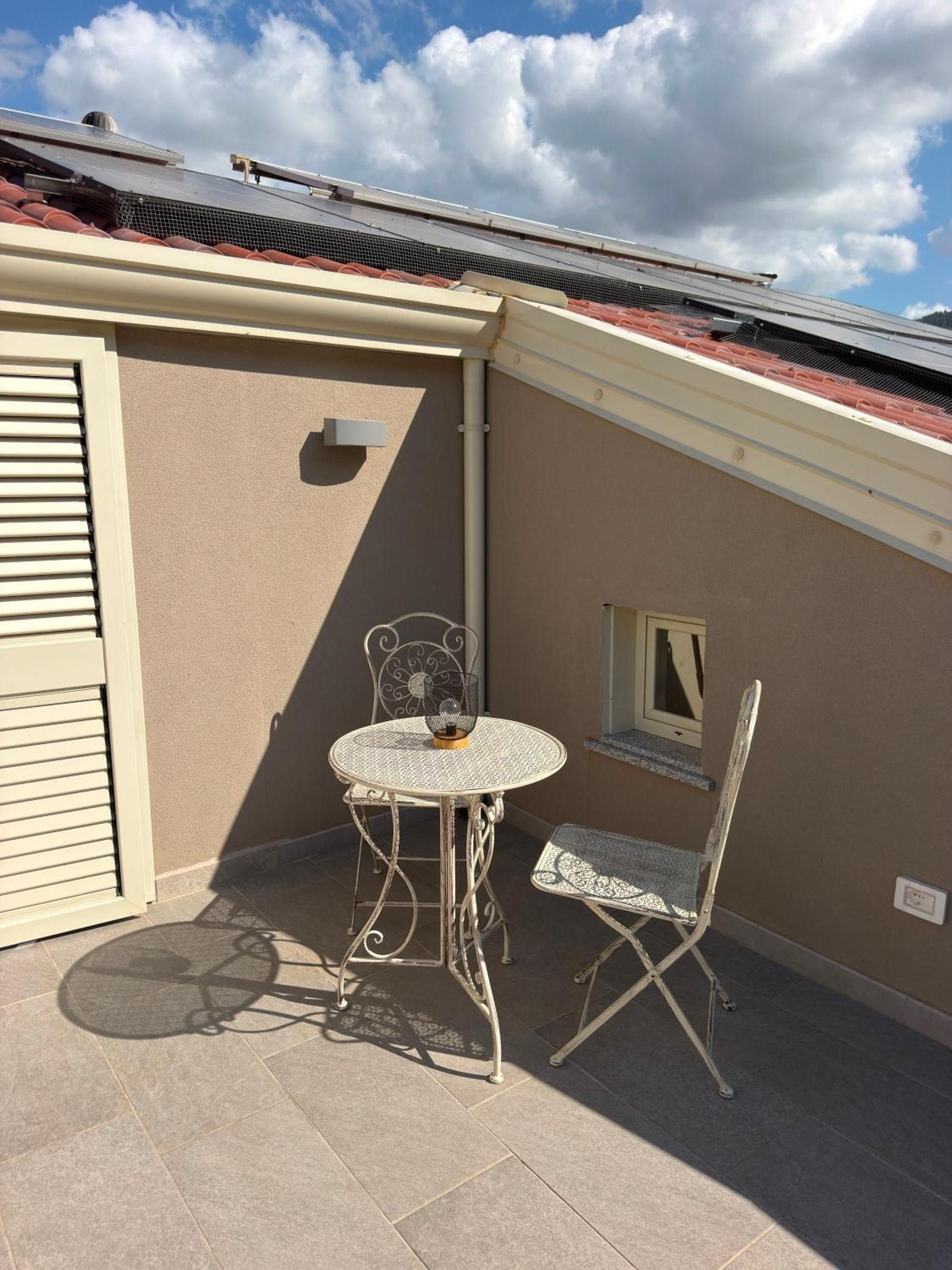 Un patio con una mesa redonda y dos sillas, una ventana pequeña y un panel solar en el techo.