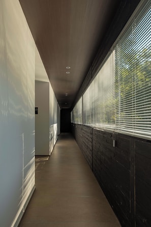 Un pasillo con techo de madera, pared de ladrillo en un lado y ventana con persianas en el otro.