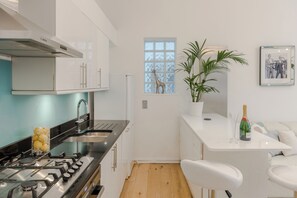 Une cuisine moderne avec une cuisinière à gaz, des armoires blanches, une fenêtre décorée avec un motif de girafe et un coin bar avec une bouteille de champagne.