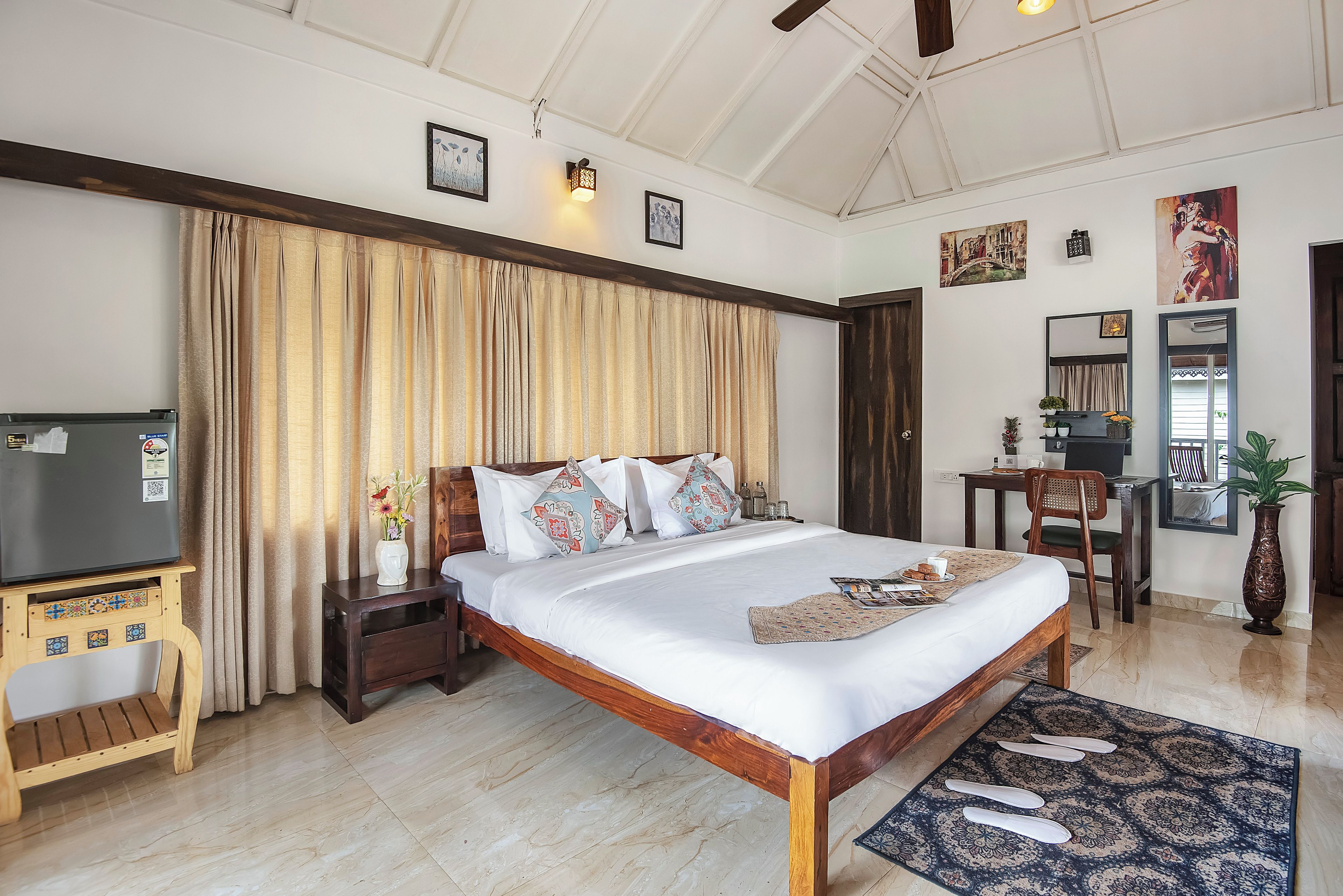 Una camera d'albergo con un letto grande, una testiera in legno, una scrivania, una sedia, un televisore e un vaso decorativo.
