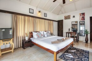 A hotel room with a large bed, wooden headboard, a small desk, a chair, a television, and a decorative vase.