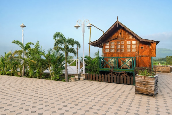 A wooden cabin with a balcony, surrounded by palm trees and a paved walkway.