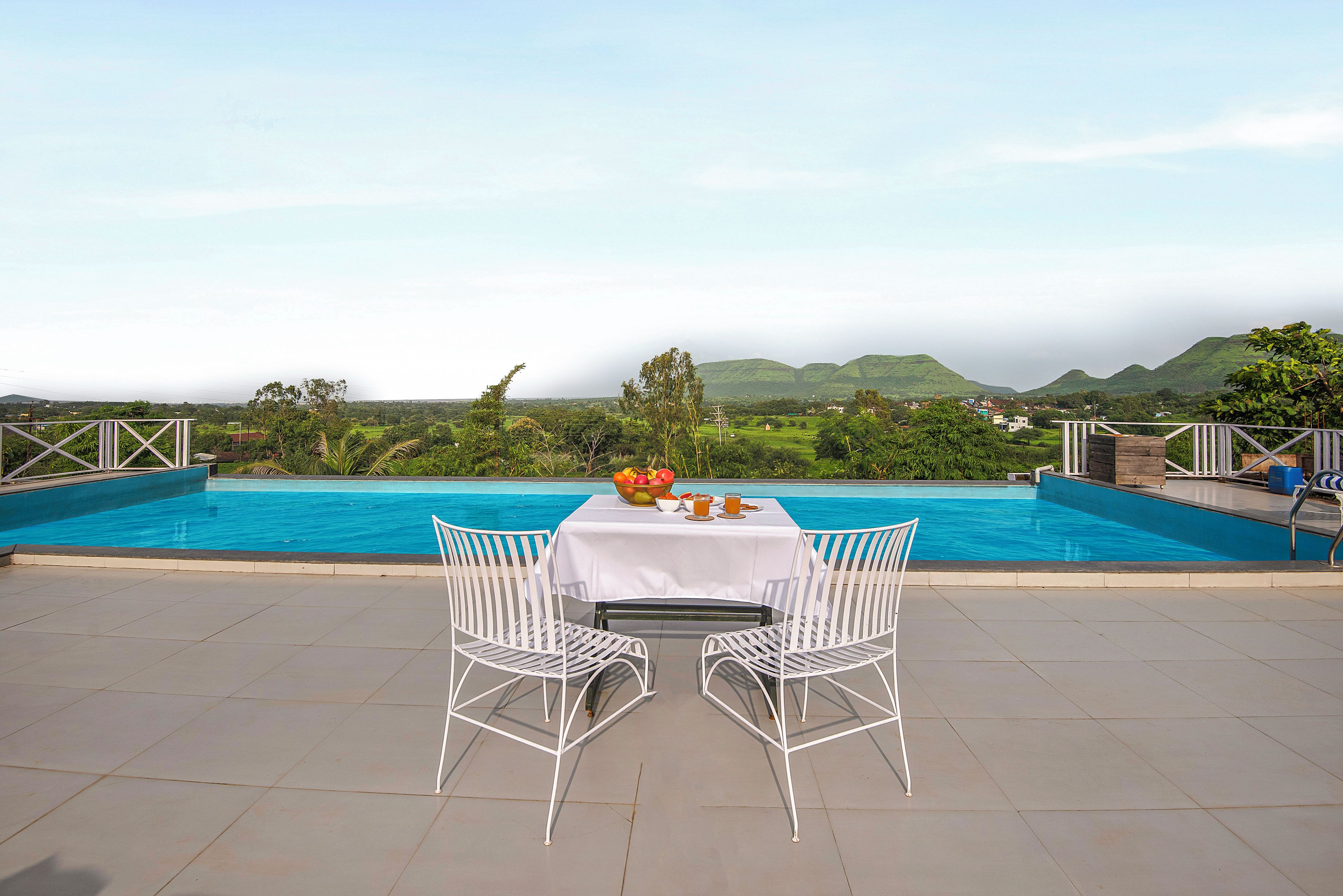 Un coin repas avec une table et des chaises donnant sur une piscine, et en arrière-plan, une vue sur des collines.