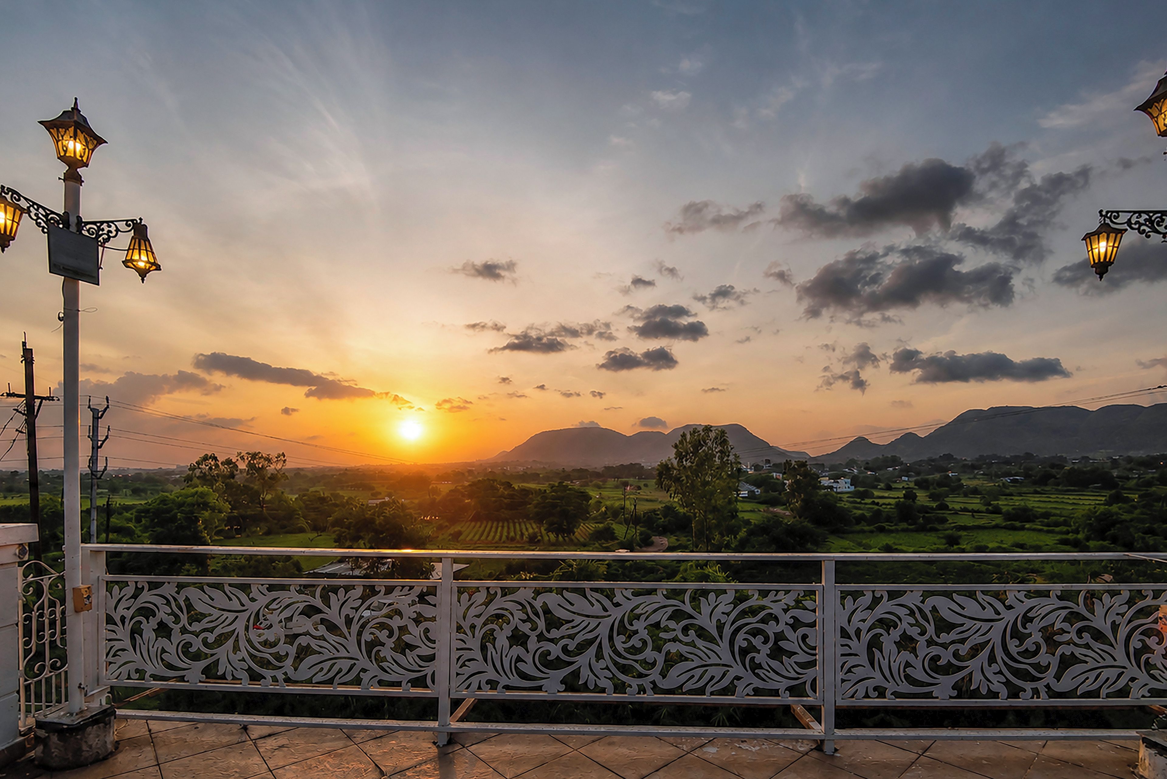 Ein Sonnenuntergangsblick von einem Balkon mit verzierten Metallgeländern und Straßenlaternen.