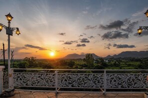 A sunset view from a balcony with ornate metal railings and street lamps.